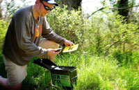 Man kneeling next to an outdoor geocache and looking at his handheld receiver