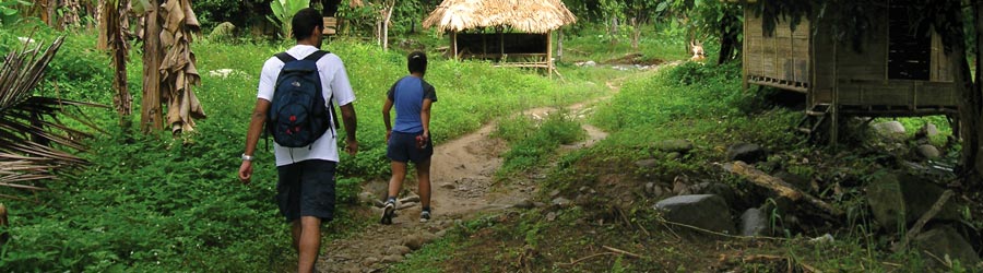 Two hikers on a path through a village in the jungle
