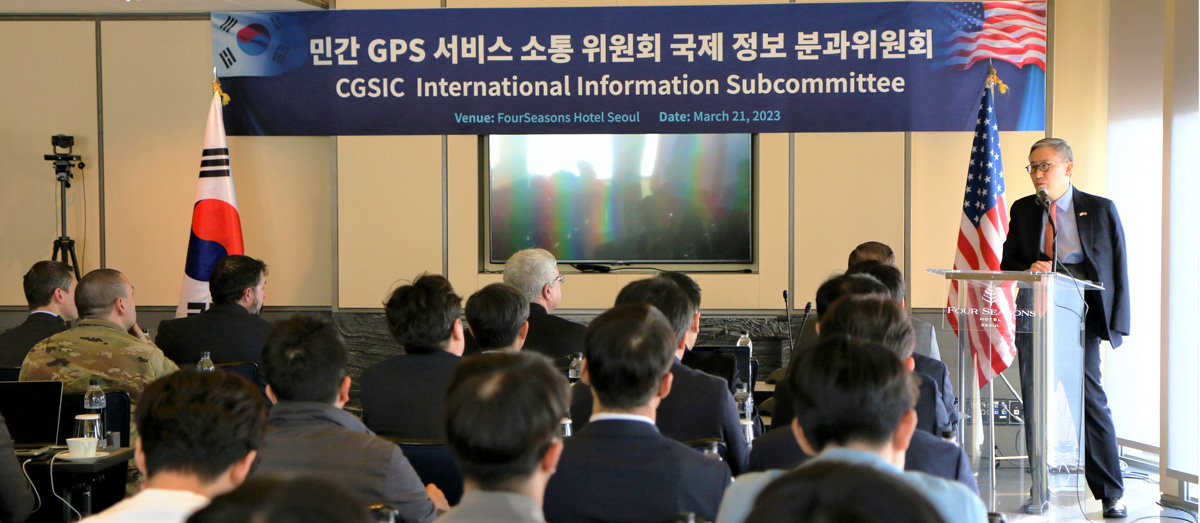 Director General Cho speaking in front of audience with presentation on screen and U.S. and Korean flags