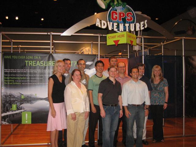 The dev team poses in front of the exhibit. GPS Adventures and Start Here sign in the background.