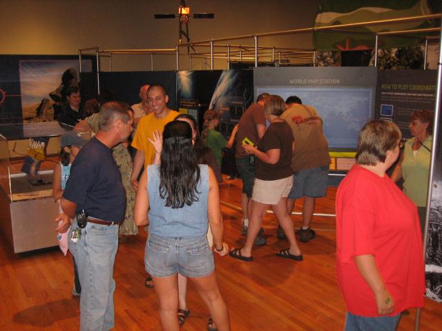 A group of people talking while others browse the exhibits in the background.