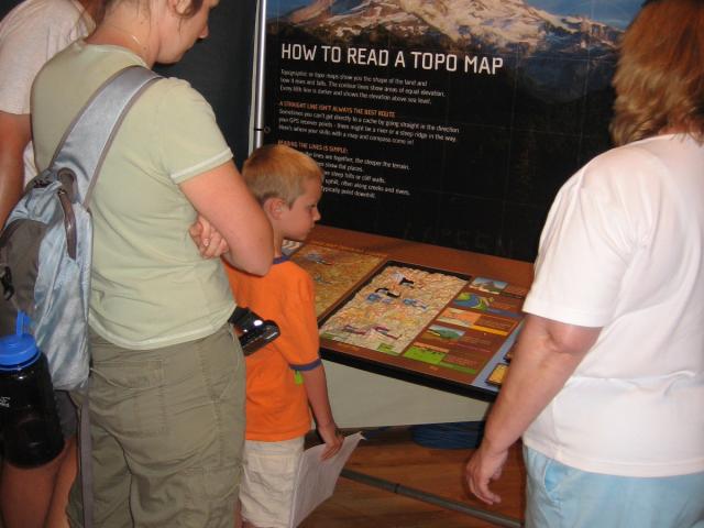 People stand in front of an exhibit on how to read topographical maps.