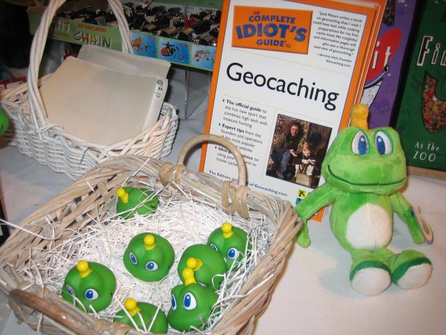 A table with a geocaching book, frog plushie, and frog head toys.