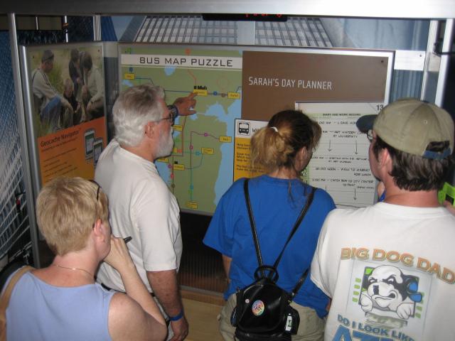 A group of people in front of an exhibit labeled Bus Map Puzzle.