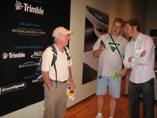 Three people talking in front of a wall with the sponsors written on it.