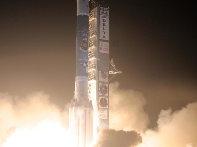 Delta II rocket launching at night with a large plume of fire and smoke from the engines.